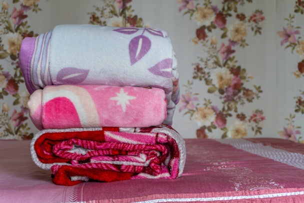白い折り畳まれた羽毛布団が横たわっています. ピンクのベッドにカラフルな毛布が積まれています. 折られたピンクの毛布 - 写真・画像
