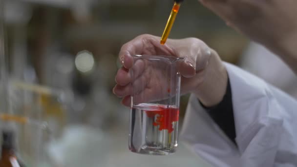 Vegyész keze vegyes anyag a vörös szín a kémcsövek. Orvos önti piros vegyi anyagok az a lombikba. Közelről 4k - Felvétel, videó