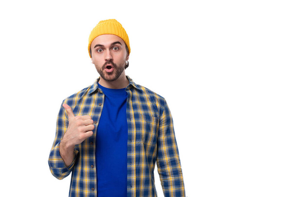 ένας νεαρός βάναυσος μελαχρινός άντρας με γενειάδα και μουστάκι σε πουκάμισο και καπέλο δείχνει τάξη. - Φωτογραφία, εικόνα