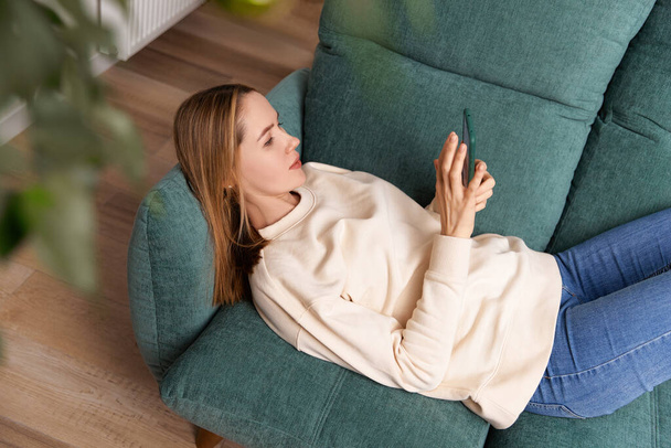 Young adult woman work with smartphone on the couch. Remote education. Work from home concept - Foto, Bild