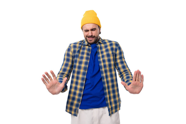 bonito surpreendido jovem hipster homem em amarelo boné e camisa joga-se as mãos no fundo branco com espaço de cópia. - Foto, Imagem