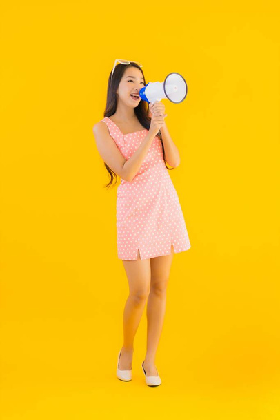 Muotokuva kaunis nuori aasialainen nainen puhuu kovaa megafonilla keltaisella eristetyllä taustalla
 - Valokuva, kuva