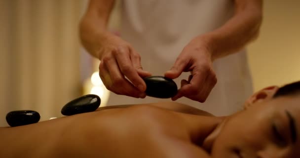 Жінка, руки та спа-масаж гарячим каменем зі шкірою та красою для термічної обробки на спині. Розслабтеся, скеля і здоров'я людини з спокоєм і детоксикацією для м'язів на ліжку салону для догляду за шкірою і тілом. - Кадри, відео