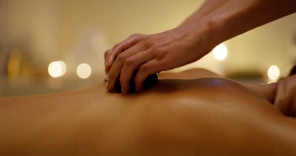 Жінка, спа-камені та масаж гарячим каменем зі шкірою та косметичними засобами для лікування болю в спині. Розслабтеся, дзен і оздоровтеся жінки з спокоєм і детоксикацією для м'язів на ліжку салону для догляду за шкірою і тілом. - Кадри, відео