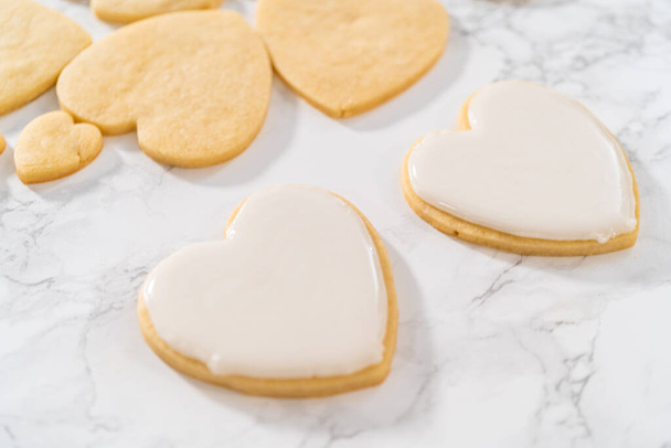 Decorating heart-shaped sugar cookies with pink and white royal icing for Valentines Day. - Photo, Image