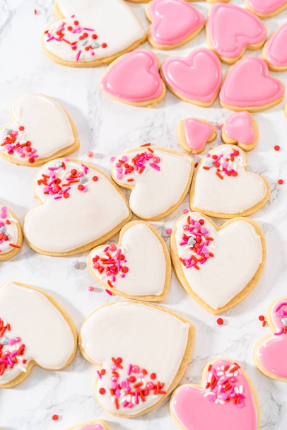 Decorating heart-shaped sugar cookies with pink and white royal icing for Valentines Day. - Photo, Image