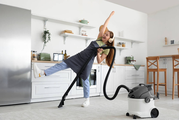 Junge Frau mit Kopfhörern saugt Teppich in Küche - Foto, Bild