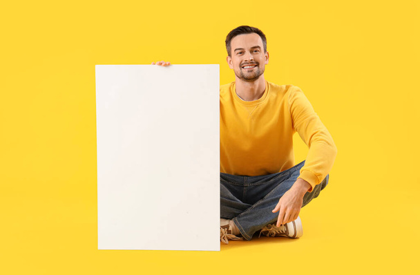Молодий чоловік з порожнім плакатом на жовтому тлі - Фото, зображення