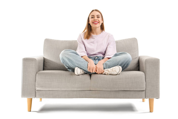 Nuori nainen istuu harmaalla sohvalla valkoista taustaa vasten - Valokuva, kuva