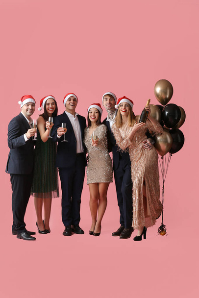 Група молодих людей у Санта-капелюхах з шампанським на рожевому фоні. Святкування Нового року - Фото, зображення