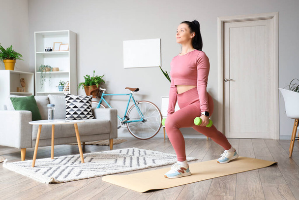 Sportieve jonge vrouw met halters training op fitness mat thuis - Foto, afbeelding