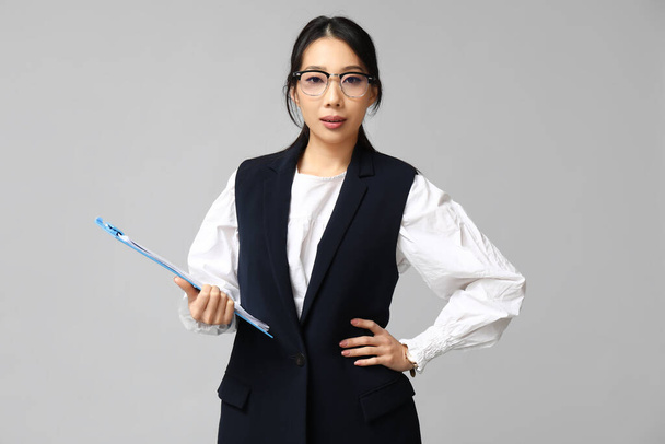 Retrato de joven empresaria asiática con portapapeles sobre fondo gris - Foto, Imagen