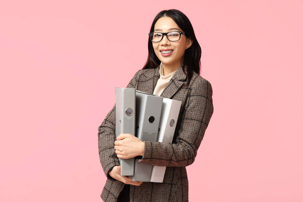 Ritratto di giovane imprenditrice asiatica con cartelle da ufficio su sfondo rosa - Foto, immagini