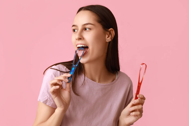 Beautiful young woman with tongue scrapers on pink background - Photo, Image