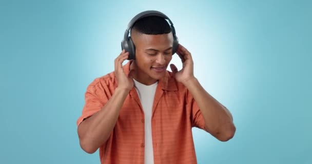 Headphones, dancing and young man in a studio listening to music, playlist or album for entertainment. Happy, smile and male model from Mexico streaming or radio with technology by blue background - Footage, Video