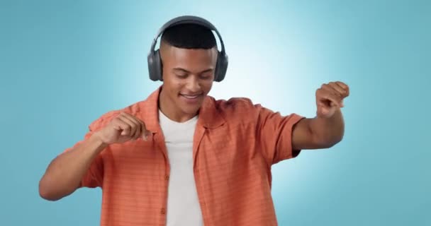 Headphones, energy and young man in a studio dancing and listening to music, playlist or album. Freedom, moving and male model from Mexico streaming a song on radio isolated by blue background - Footage, Video