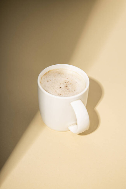Cappuccino in einer weißen Tasse mit Lichtstrahlen auf beigem Hintergrund - Foto, Bild