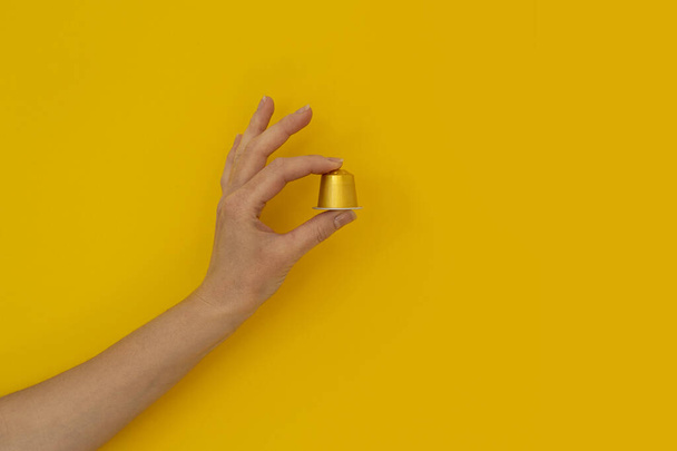 Mano de mujer sosteniendo una cápsula de café sobre un fondo amarillo. - Foto, imagen