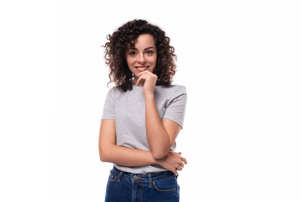 positive selbstbewusste, helle junge, schlanke, brünette Frau mit lockiger Frisur gekleidet in einem grauen T-Shirt auf weißem Hintergrund mit Kopierraum. - Foto, Bild