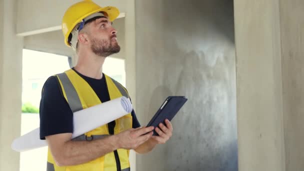 Male architect foreman watches progress by looking at construction blueprints holds laptop looks at interior design and details under construction in housing project looking at camera gives thumbs up. - Footage, Video