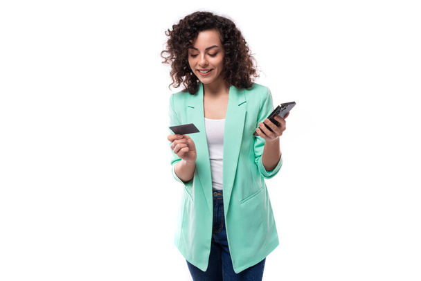 jovem modelo feminino branco magro com cabelo preto encaracolado usa dados de smartphone e cartão para pagar compras on-line. - Foto, Imagem