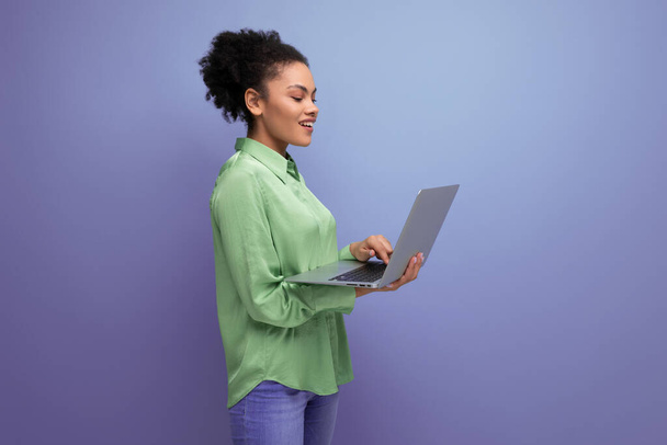 successful young bright latin woman dressed in a green blouse works remotely with a laptop. - Photo, Image