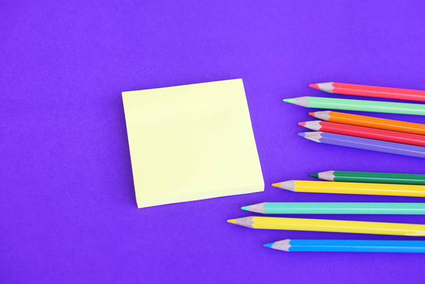 Цветные карандаши и бумажный блокнот на фиолетовом фоне. Концепция, учебные материалы, искусство. Принимая к сведению, стройте планы, напоминание.             - Фото, изображение