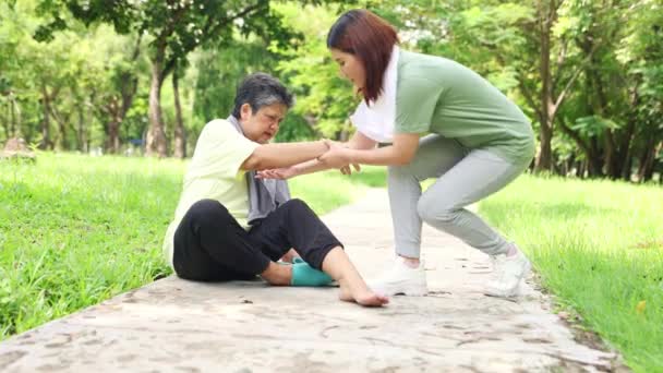 Figlia grata aiuta la madre il cui piede fa male durante l'esercizio in giardino per alzarsi lentamente e camminare in modo sicuro: concetto di assistenza sanitaria anziani. - Filmati, video