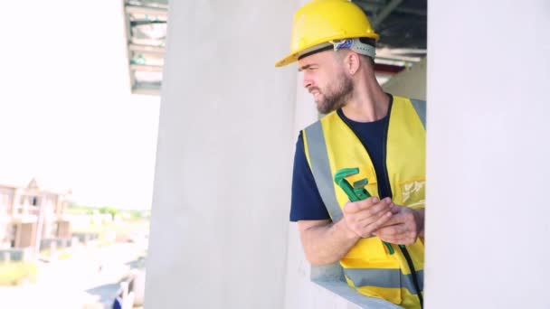 Hombre trabajador saluda a compañeros de trabajo en el sitio de construcción mientras trabaja en el segundo piso de una casa en un gran proyecto. - Metraje, vídeo