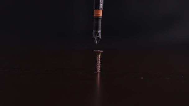Uma chave de fenda prendendo firmemente um parafuso em uma superfície de madeira, com partículas voando ao redor enquanto penetra no material. - Filmagem, Vídeo
