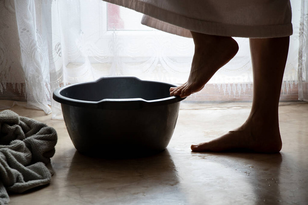 Een meisje in een badjas wast haar voeten in een kom in de slaapkamer op de vloer, wast haar voeten, hygiëne, voetverzorging - Foto, afbeelding
