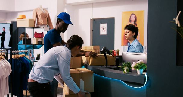 African american courier showing shipping report, discussing packages distribution in modern boutique. Stylish employee working at online orders, preparing trendy clothes for delivery in shopping mall - Photo, Image