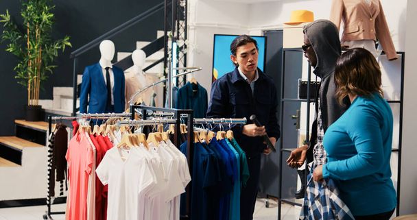 Kradnący sklepy próbujący ukraść modny towar z centrum handlowego, złapany przez azjatyckiego ochroniarza. Afrykańska para kłócąca się z bodyguradem, próbująca uniknąć oskarżenia w sklepie odzieżowym - Zdjęcie, obraz