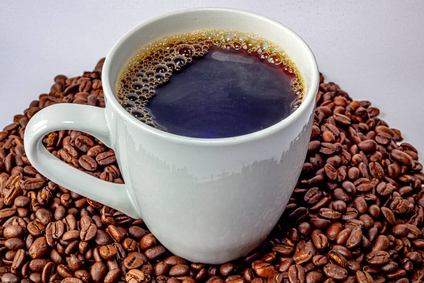 Ένα φλιτζάνι καφέ πάνω σε ένα σωρό φρεσκοψημένου καφέ. - Φωτογραφία, εικόνα