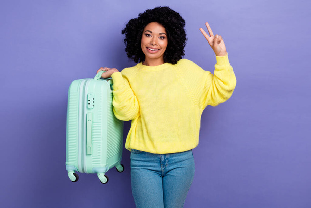 Photo of cheerful woman with afro hairdo dressed sweater showing v-sign symbol holding luggage isolated on violet color background. - Valokuva, kuva