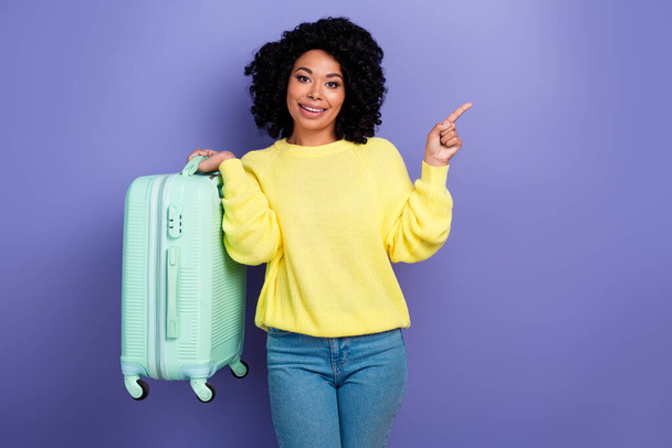 Portrait of pleasant person with chevelure wear pullover hold baggage indicating at offer empty space isolated on purple color background. - Foto, Imagem