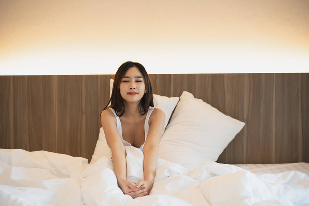 Asyalı bir kadın yatakta uzanıyor, esniyor ve mutlu bir kadın uykusundan sonra uyanıyor, dinleniyor ve evde dinleniyor. Dinleniyor, gülümsüyor ve yatak odasında geriniyor, huzurlu, keyifli konsept. - Fotoğraf, Görsel
