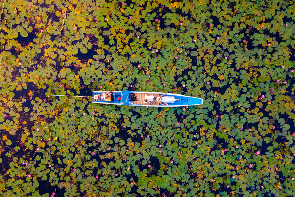 Das Meer aus rotem Lotus, Lake Nong Harn, Udon Thani, Thailand, ein Paar Männer und Frauen in einem Boot bei Sonnenaufgang am Roten Lotussee im Isaan - Foto, Bild