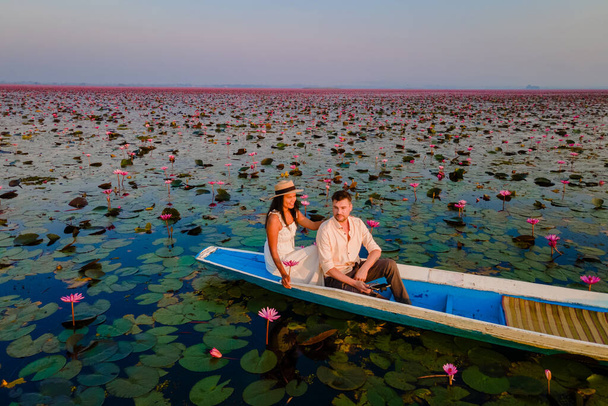 Das Meer aus rotem Lotus, Lake Nong Harn, Udon Thani, Thailand, ein Paar Männer und Frauen in einem Boot bei Sonnenaufgang am Roten Lotussee im Isaan bei Sonnenaufgang - Foto, Bild
