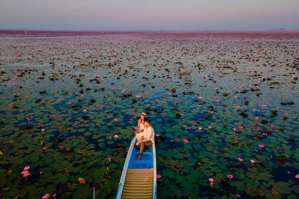 Drohnen-Luftaufnahme am Meer des roten Lotus, Lake Nong Harn, Udon Thani, Thailand, ein Paar Männer und Frauen in einem Boot bei Sonnenaufgang am Roten Lotus See in der Isaan - Foto, Bild