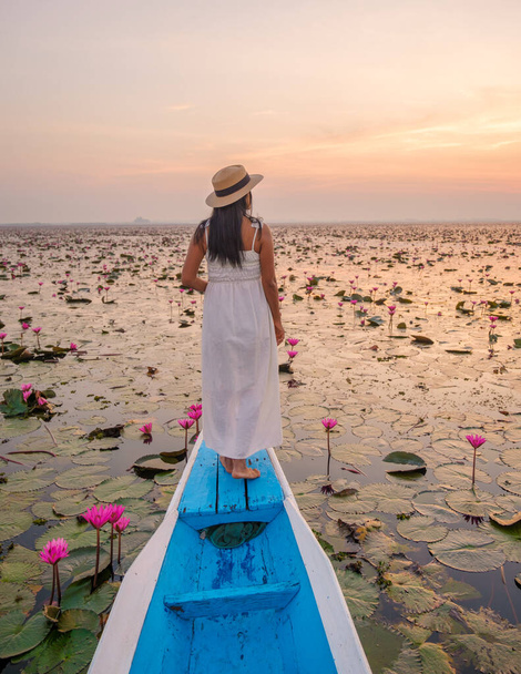 Das Meer aus rotem Lotus, Lake Nong Harn, Udon Thani, Thailand. Asiatin mit Hut und Kleid auf einem Boot am roten Lotussee im Isaan bei Sonnenaufgang - Foto, Bild