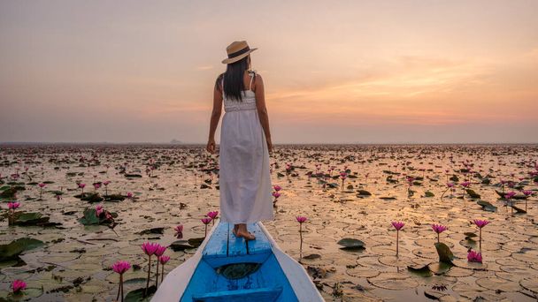 Das Meer aus rotem Lotus, Lake Nong Harn, Udon Thani, Thailand. Asiatische Thailänderin mit Hut und Kleid auf einem Boot am Roten Lotussee im Isaan - Foto, Bild