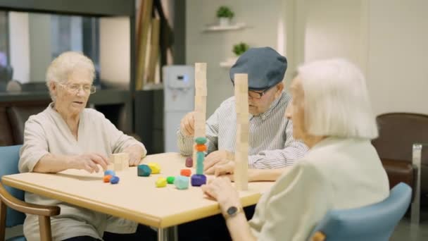 Video de tres personas mayores jugando juegos de mesa de habilidad en un hogar de ancianos - Imágenes, Vídeo