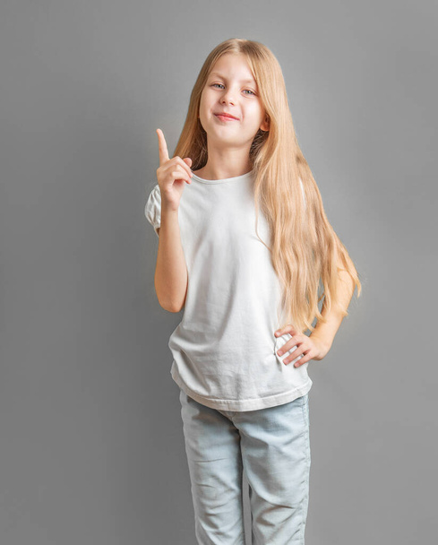 Портрет милой маленькой девочки с длинными светлыми волосами, прямой палец вверх  - Фото, изображение