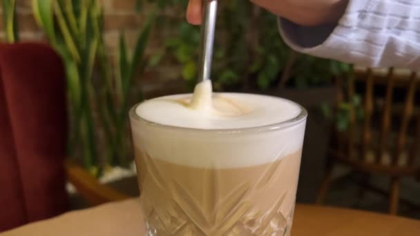Eine Frau dreht in einem Café eine Untertasse und ein Glas mit Latte um, auf der Untertasse liegt ein Keks in Form von Kaffeebohnen. Hochwertiges 4k Filmmaterial - Filmmaterial, Video