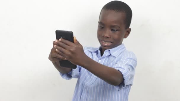 Niño sosteniendo y jugando con un teléfono móvil aislado sobre fondo blanco. Aprendizaje infantil para usar dispositivos electrónicos modernos - Imágenes, Vídeo