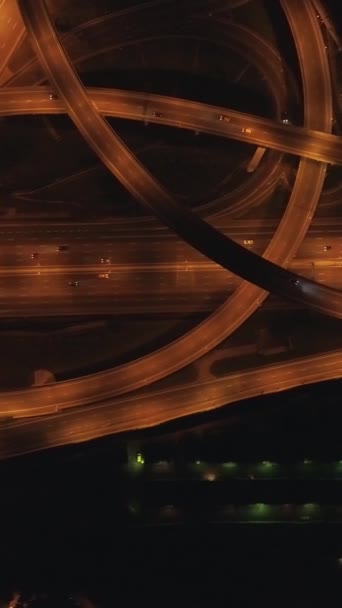 夜間の複雑な道路交差点と車の交通を照らしました. ドローンは左に飛んでいる. 垂直ショット。 バーティカルビデオ - 映像、動画