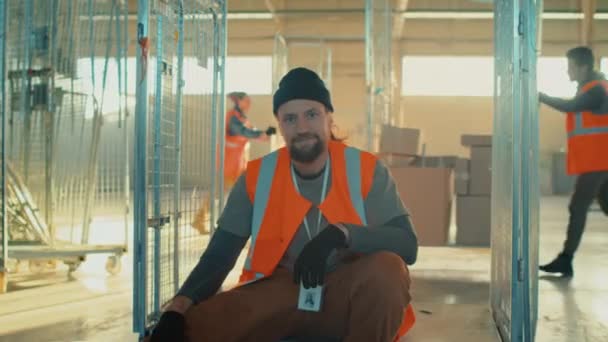 Portrait de ralenti moyen d'un homme travailleur d'entrepôt de distribution caucasien assis sur des bosseurs dans une salle de stockage spacieuse et regardant la caméra pendant la journée de travail - Séquence, vidéo