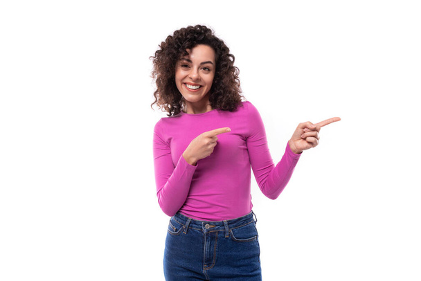 κομψή λεπτή νεαρή σγουρή μελαχρινή γυναίκα ντυμένη με λιλά ζιβάγκο δείχνει το δάχτυλό της στον άδειο χώρο. - Φωτογραφία, εικόνα