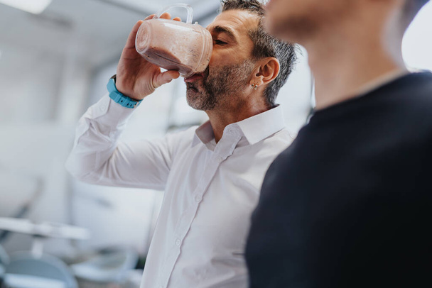 İş adamı ofis mutfağında protein içeceğini yudumlarken sağlığın merkezi bir konuma geliyor.. - Fotoğraf, Görsel